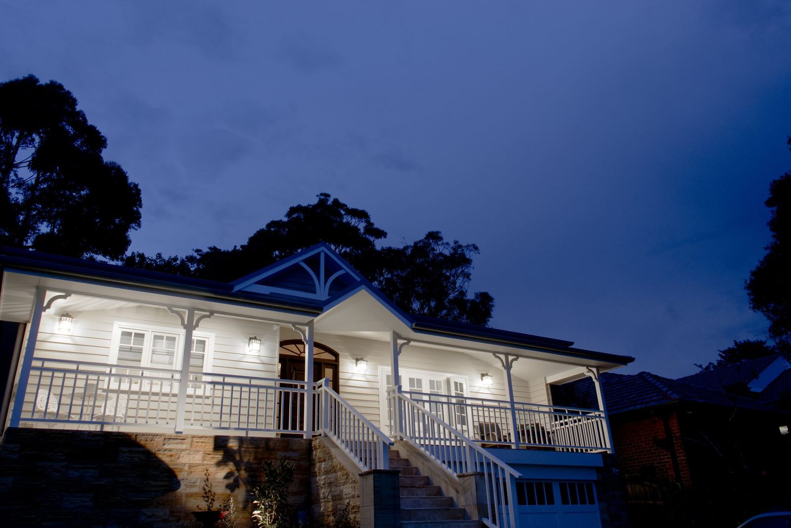 Balgowlah — dusk view of the weatherboard home with a lit veranda and garden, built by HP Constructions with Scope Architects