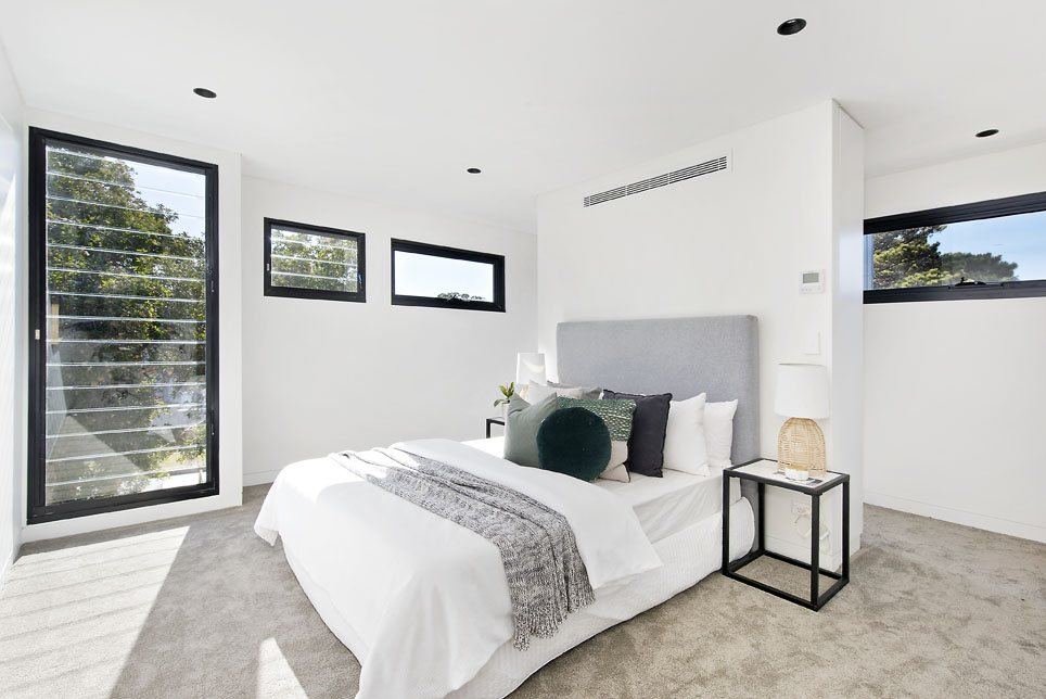 Bondi — bedroom with upholstered bed, grey carpet and black-framed windows, built by HP Constructions with Arkhaus