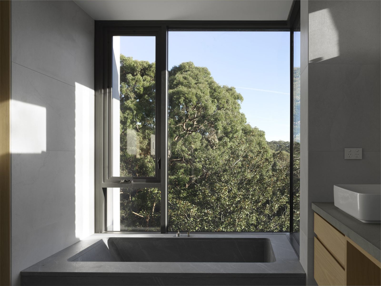 Castle Cove — bathroom with stone bath beneath full-height window overlooking trees, built by HP Constructions with Dieppe Design