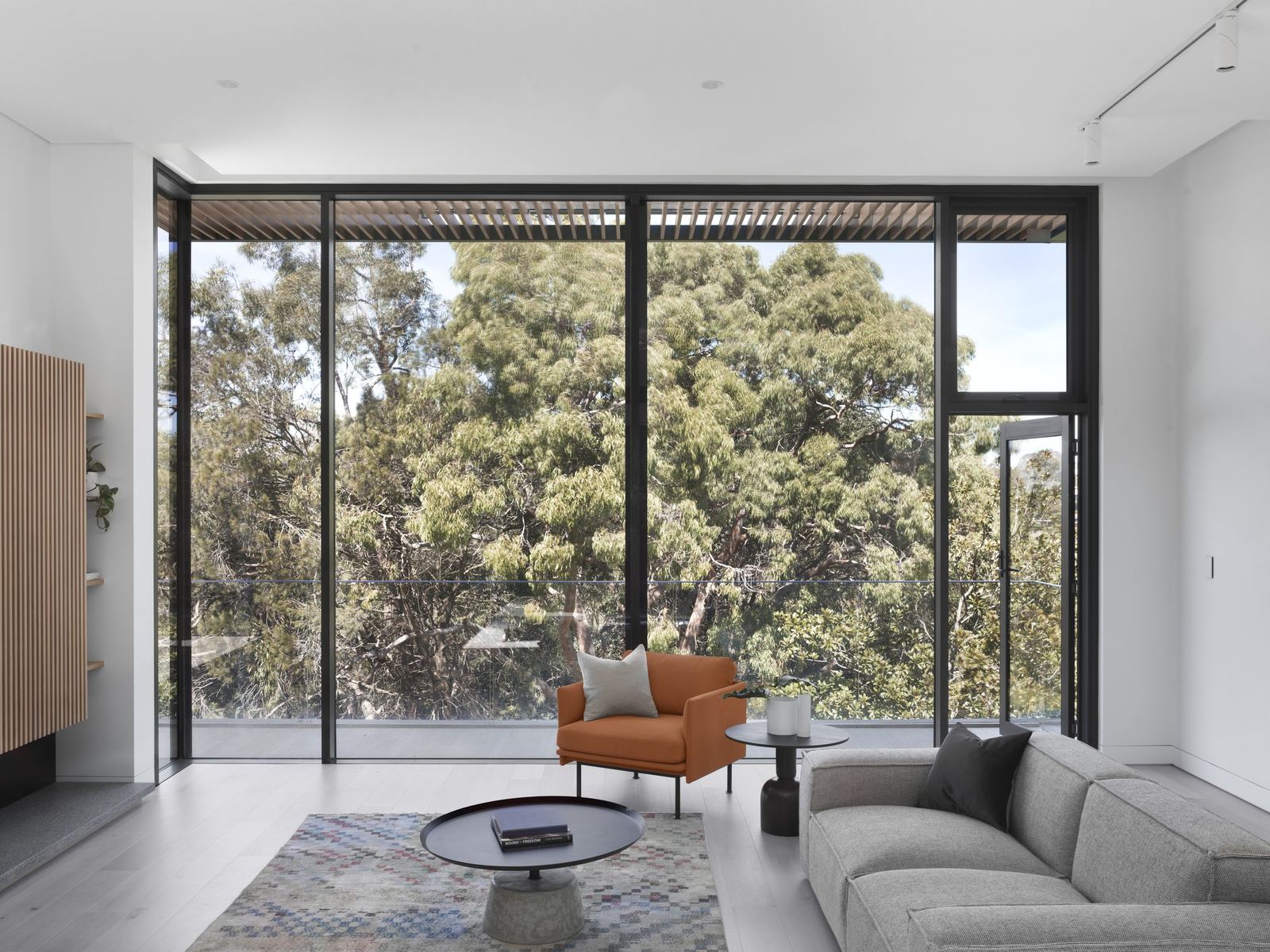 Castle Cove — living room with full-height glazing to trees, tan armchair and grey sofa, built by HP Constructions with Dieppe Design