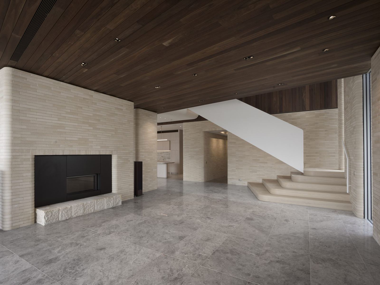Castlecrag — living area with fireplace, curved travertine stair and stone floor, built by HP Constructions with FJC Studio