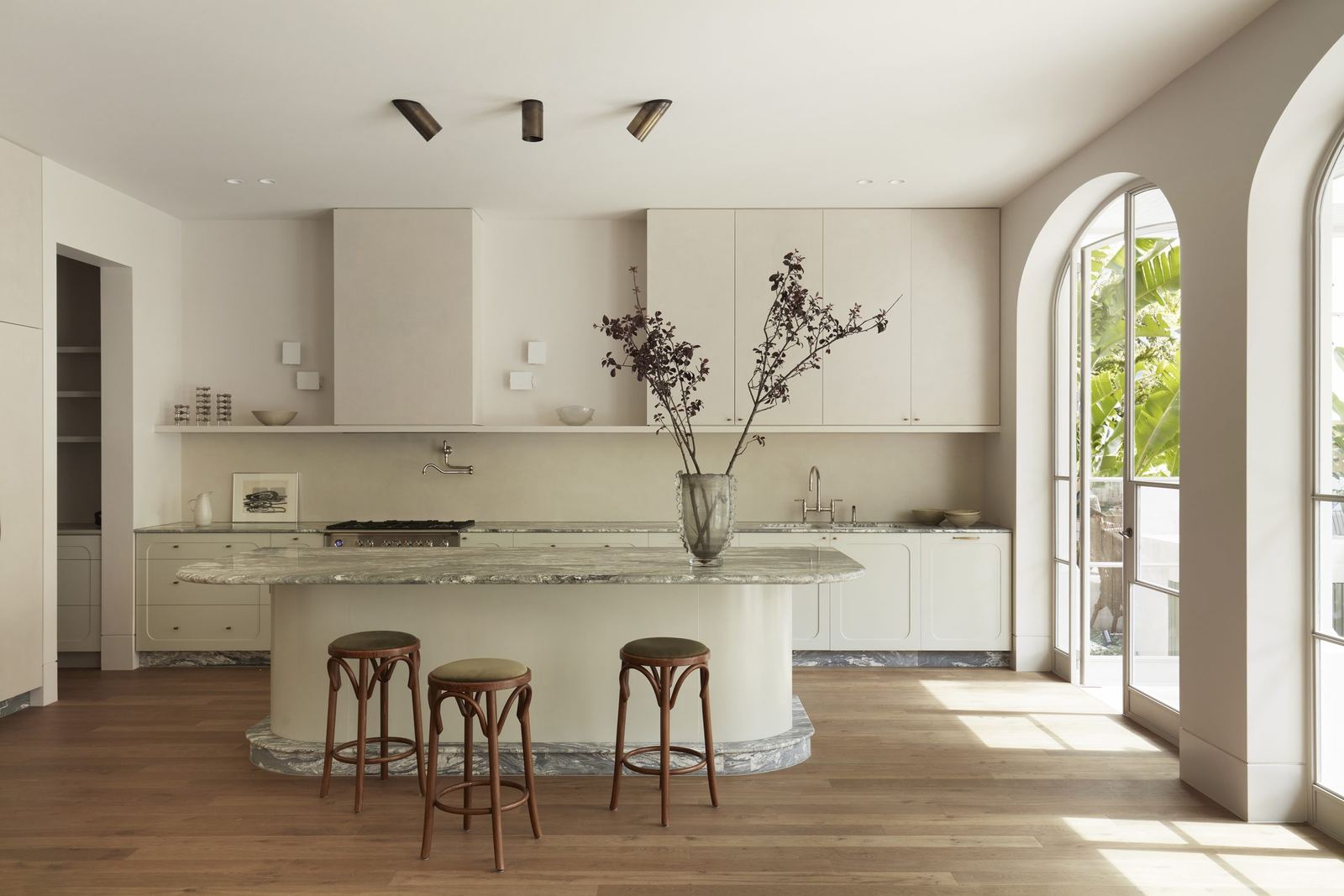Darling Point — kitchen with curved stone island, timber stools and arched garden doorway, built by HP Constructions with Hancock Architects