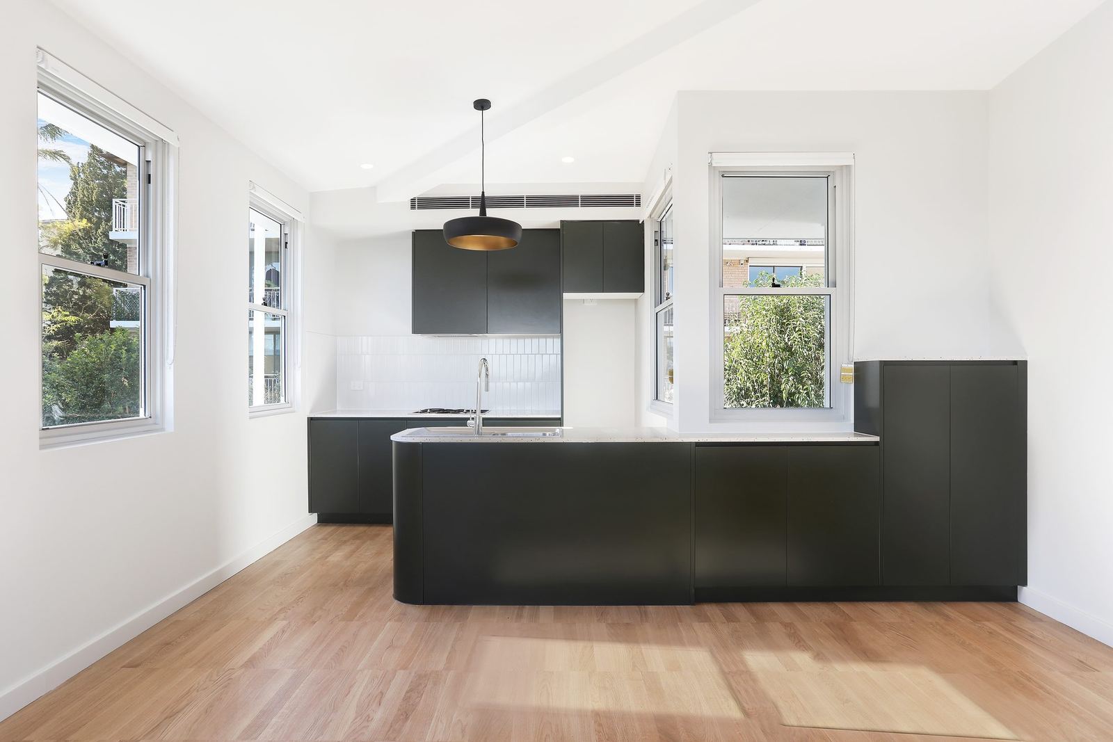 Queens Park Apartments — empty apartment kitchen with black island and timber floor, built by HP Constructions with Ignite Architects