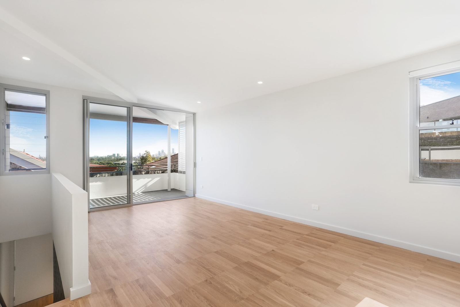 Queens Park Apartments — vacant living room with sliding balcony door and timber floor, built by HP Constructions with Ignite Architects