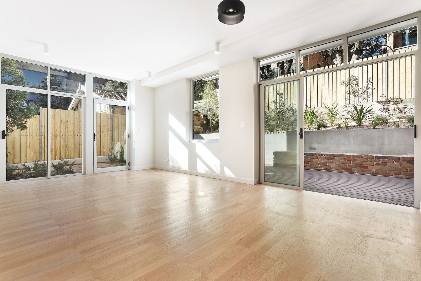 Queens Park Apartments — living room opening through glass doors to paved courtyard, built by HP Constructions with Ignite Architects