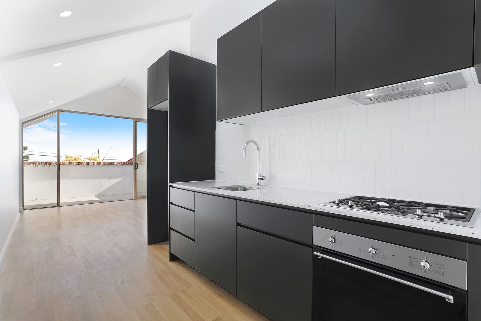 Queens Park Apartments — black kitchen cabinetry with gas cooktop and white splashback, built by HP Constructions with Ignite Architects