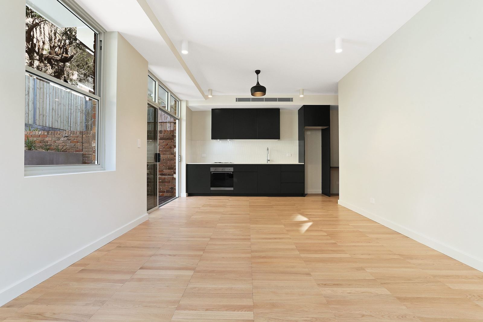 Queens Park Apartments — open living space with black kitchen and exposed brick wall, built by HP Constructions with Ignite Architects