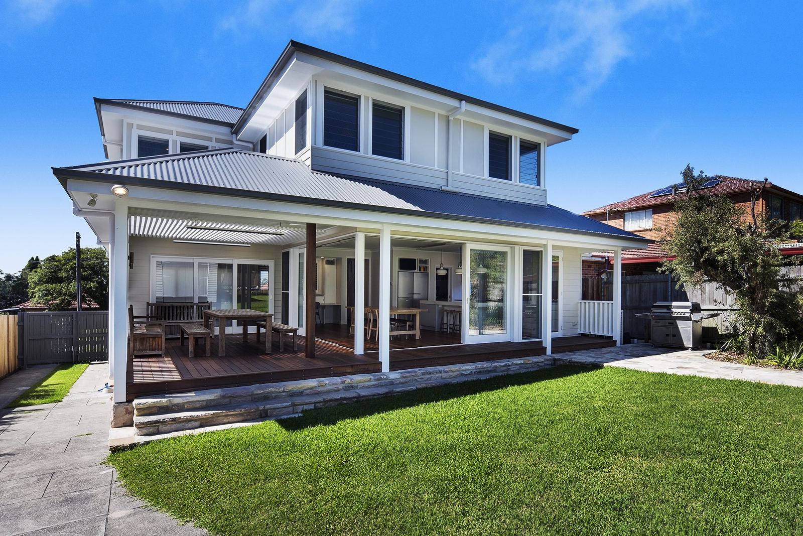 Seaforth — rear exterior with covered deck, lawn, sandstone paving and outdoor dining, built by HP Constructions with Playoust Churcher
