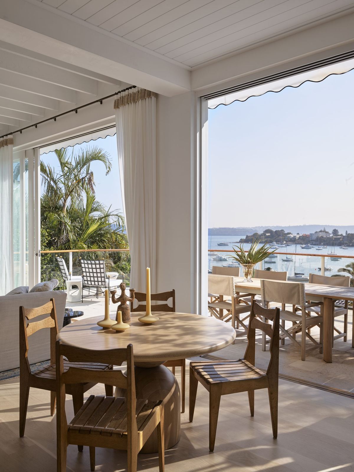 Vaucluse — dining area with round timber table opening to terrace and bay, built by HP Constructions with Alexander & Co